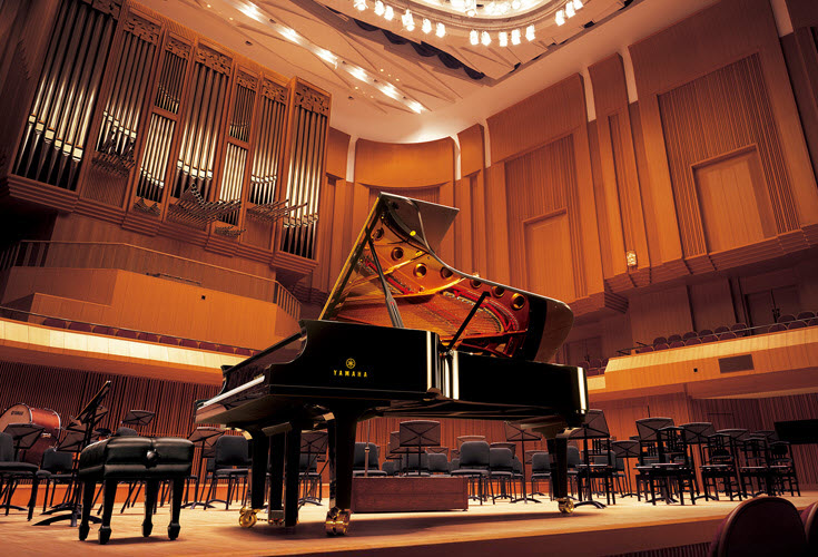 Yamaha CFX A grand piano alone on a stage in a concert hall.