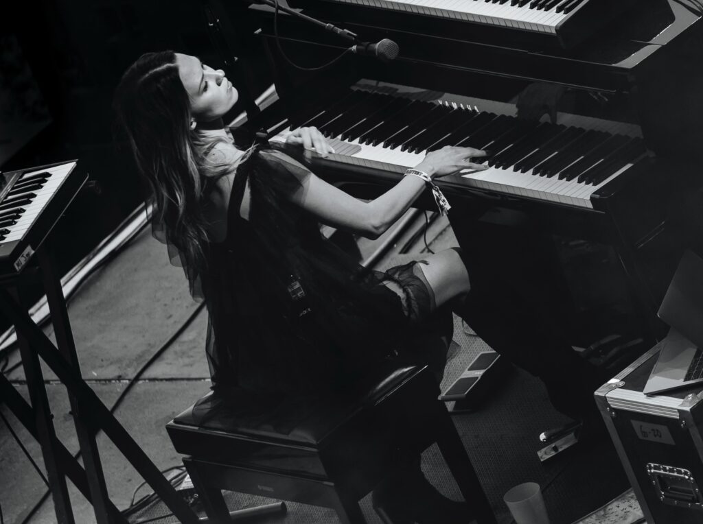 Black and white image of a young woman seen sitting at Yamaha concert grand piano on a darkened stage. 