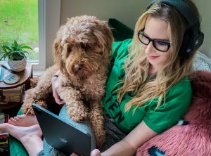 A girl wearing headphones with a dog on her lap watching a movie on a tablet.