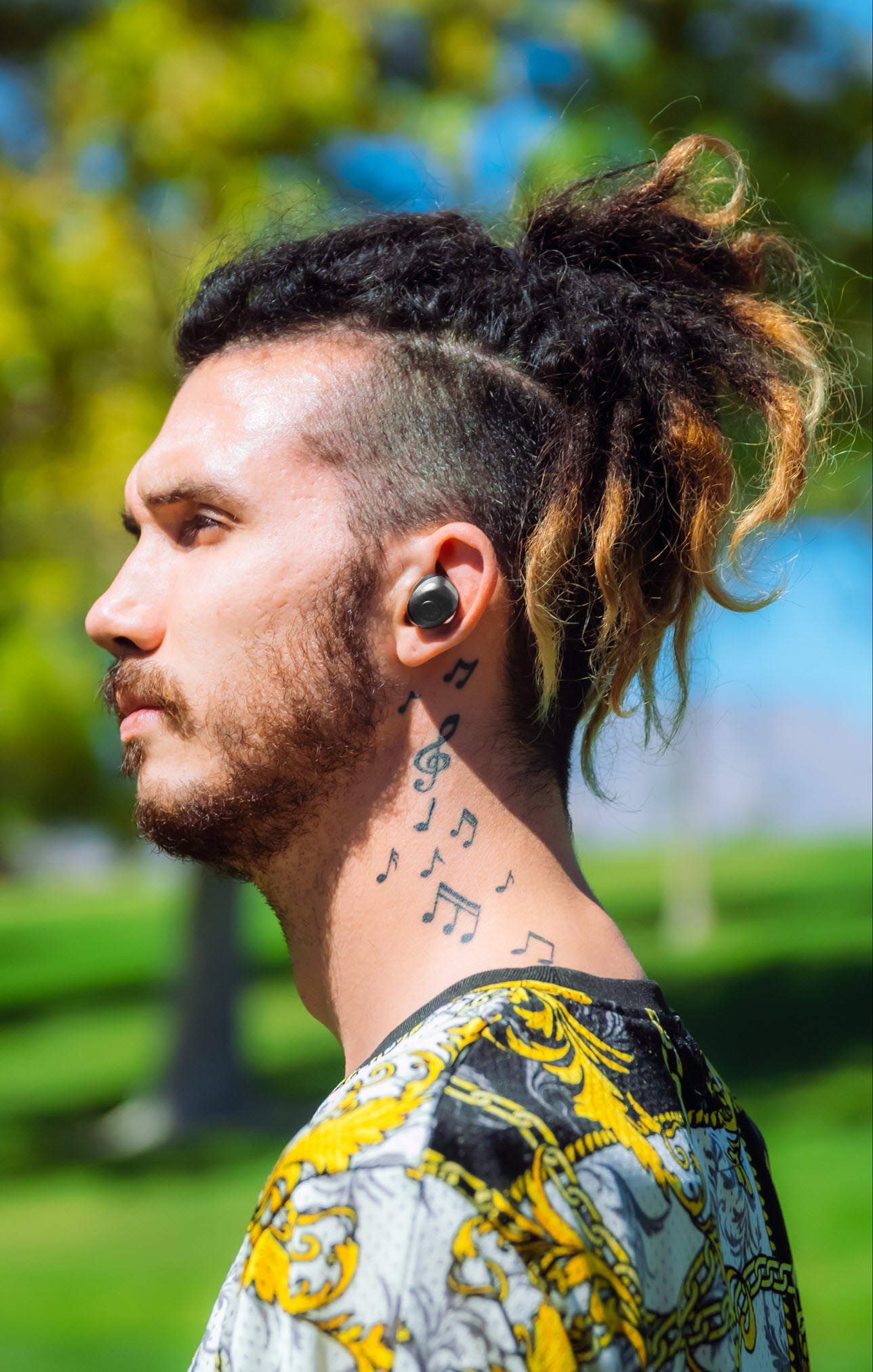 Credit-officialjackel-72DPI Young man with dreads and body art wearing earbuds. Seen in profile.