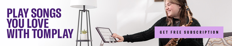 A smiling woman holding a saxophone and touching a tablet.