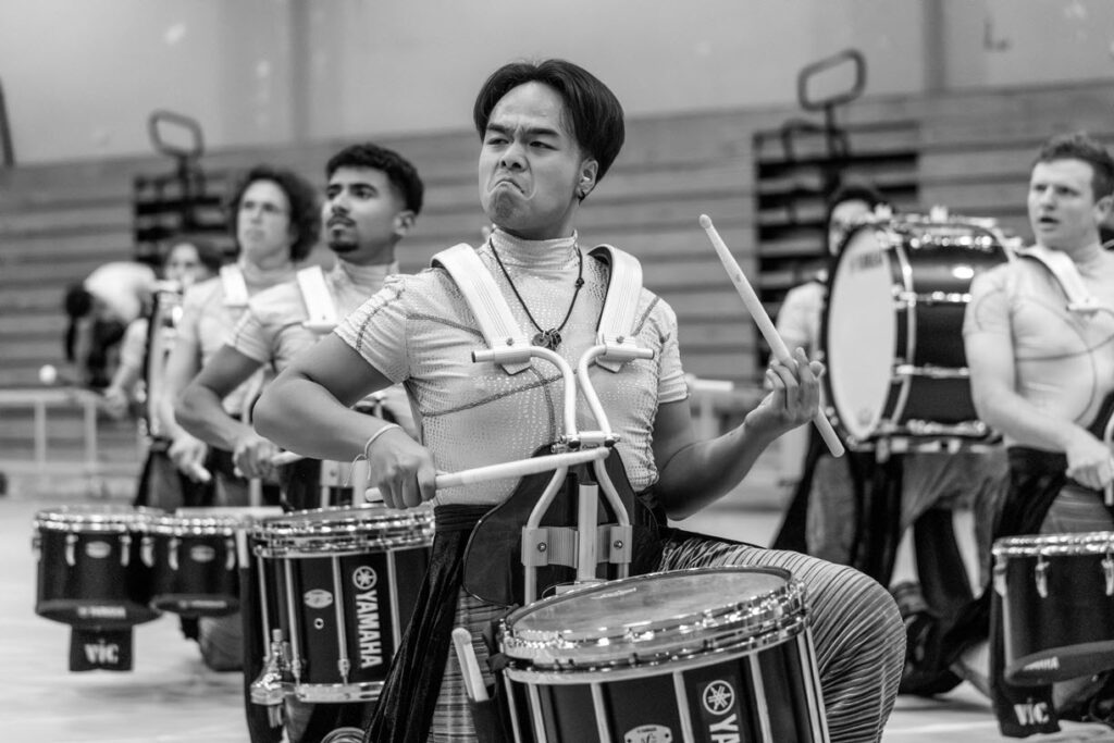 WGI_History_Blog_3 Closeup of snare drummers in a marching band performing in a gym.